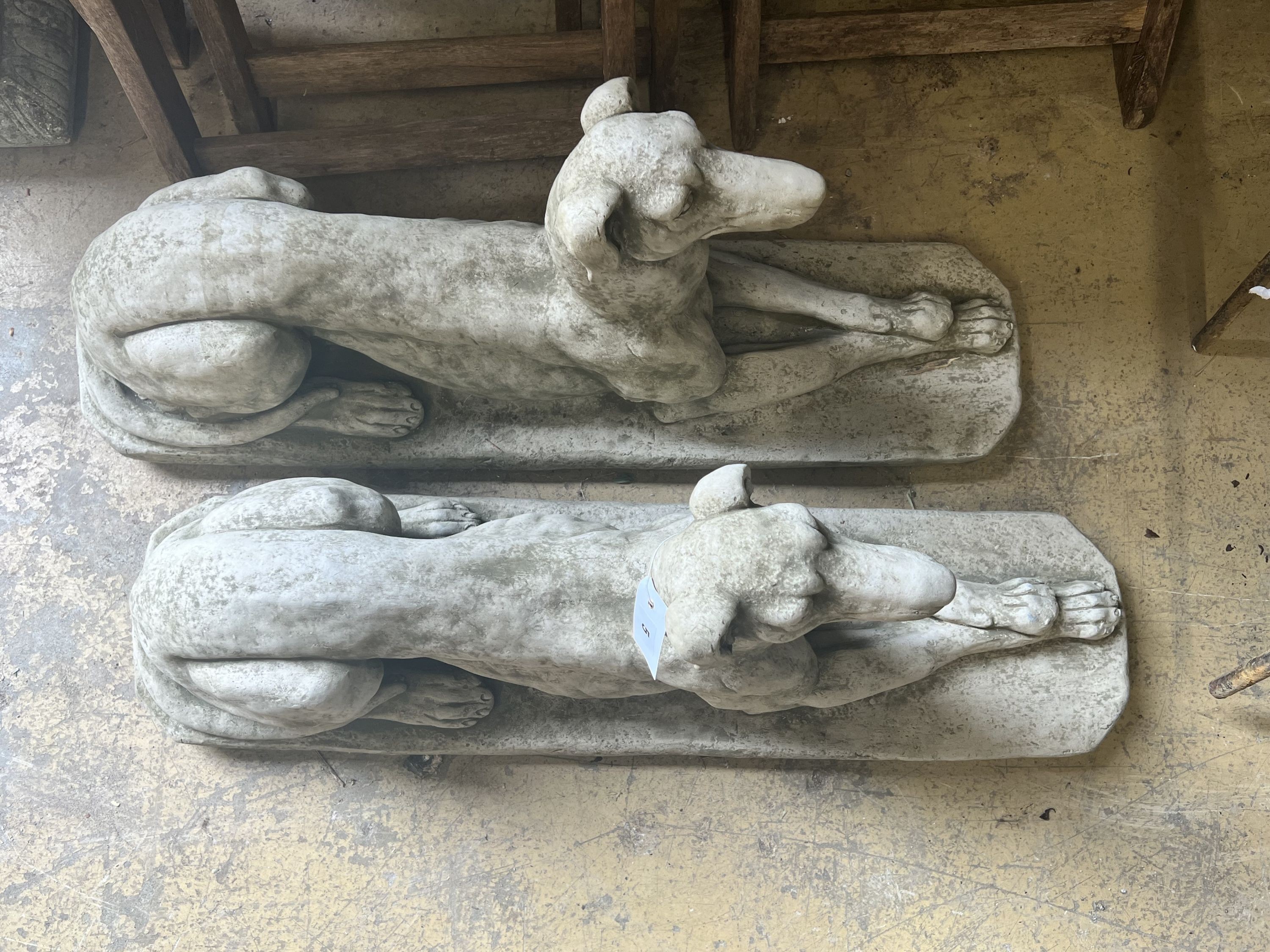 A pair of reconstituted stone recumbent greyhound ornaments, length 82cm